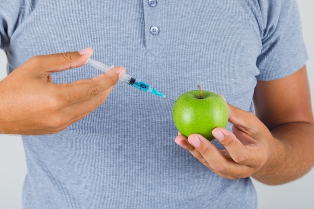 Jonge man uitvoeren van experiment door injectie in appel in grijs t-shirt