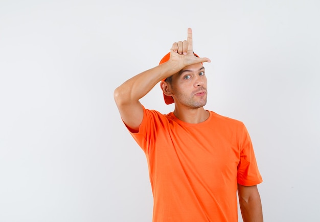 Jonge man verliezer teken weergeven op zijn voorhoofd in oranje t-shirt en pet vooraanzicht.