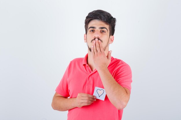 Jonge man verzendt kus met de hand in t-shirt en ziet er schattig uit, vooraanzicht.