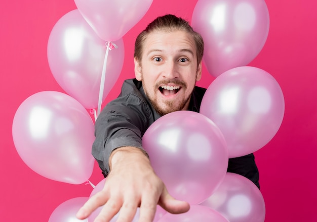 Jonge man viert verjaardagsfeestje met ballonnen verbaasd en verrast over roze