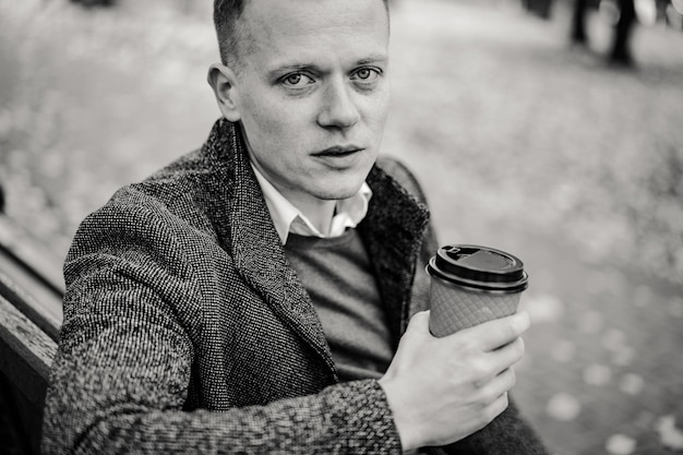 Jonge man wandelen in de herfststad met een glas koffie