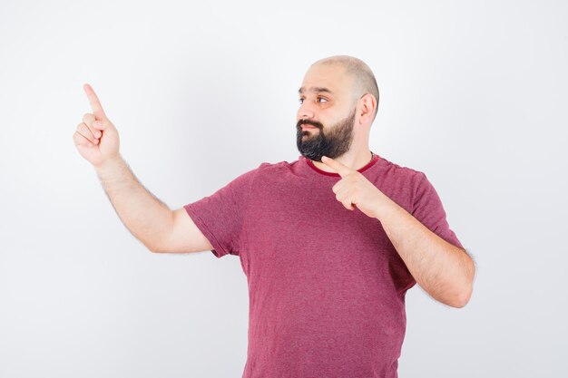 Jonge man wijst naar de linkerbovenhoek in t-shirt en kijkt gefocust. vooraanzicht.