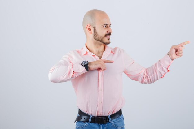 Jonge man wijst naar de rechterkant in shirt, spijkerbroek en ziet er vrolijk uit. vooraanzicht.