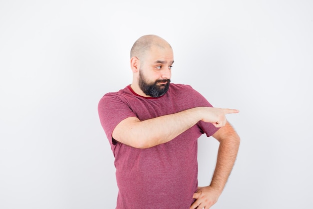 Jonge man wijst naar de rechterkant in t-shirt en kijkt verbaasd. vooraanzicht.