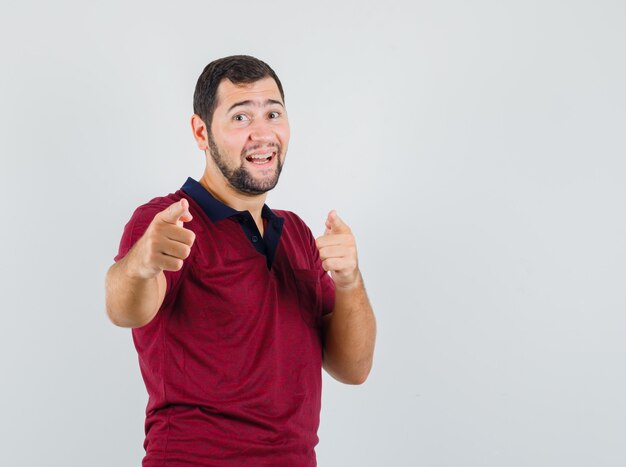 Jonge man wijst naar de voorkant in rood t-shirt en kijkt gelukkig, vooraanzicht.