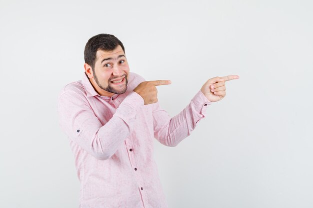 Jonge man wijst naar de zijkant in roze shirt en kijkt optimistisch