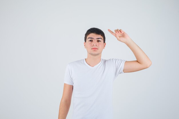 Jonge man wijst opzij in t-shirt en kijkt voorzichtig. vooraanzicht.