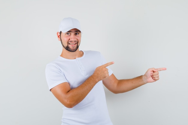 Jonge man wijst opzij in wit t-shirt en kijkt tevreden, vooraanzicht.