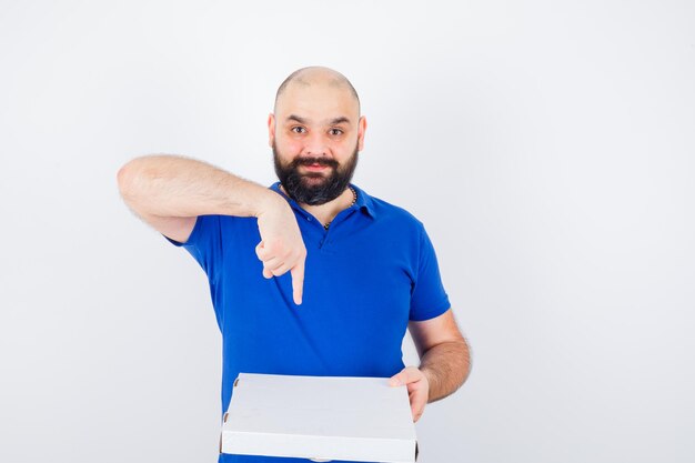 Jonge man wijst pizzadoos in t-shirt en ziet er vrolijk uit. vooraanzicht.