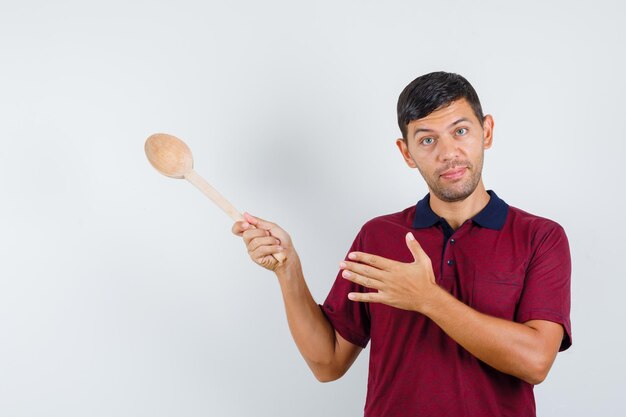 Jonge man wijst weg met houten lepel in t-shirt en ziet er zacht uit, vooraanzicht.