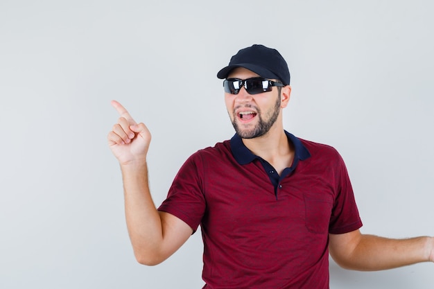 Jonge man wijst weg terwijl hij iets in t-shirt, zonnebril vraagt en klaar kijkt. vooraanzicht.