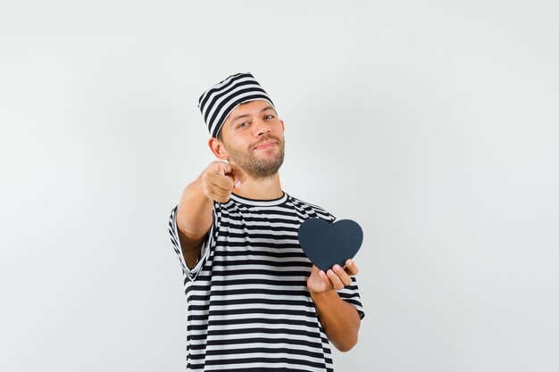 Jonge man wijzend op camera huidige doos in gestreepte t-shirt hoed te houden en op zoek vrolijk