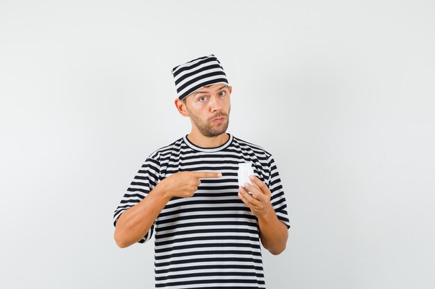 Jonge man wijzend op fles pillen in gestreepte t-shirt hoed