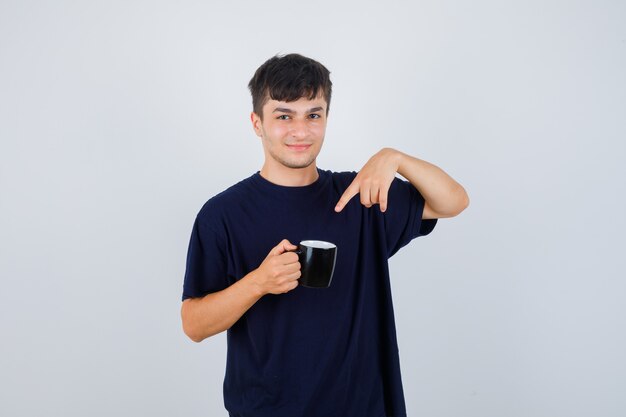 Jonge man wijzend op kopje thee in zwart t-shirt en kijkt zelfverzekerd, vooraanzicht.
