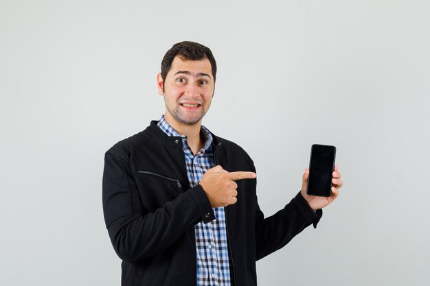 Jonge man wijzend op mobiele telefoon in shirt, jasje en vrolijk op zoek