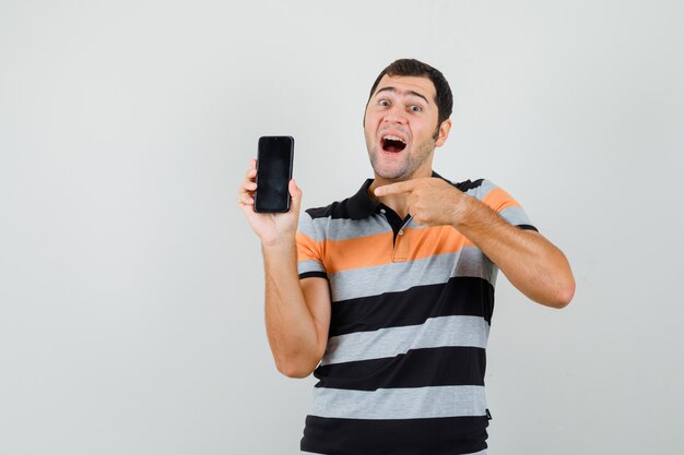 Jonge man wijzend op telefoon in t-shirt en kijkt tevreden