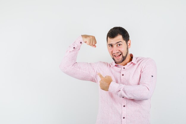 Jonge man wijzend op zijn spieren in roze shirt en op zoek zelfverzekerd