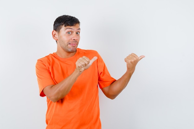 Jonge man wijzende duimen weg in oranje t-shirt en op zoek bewust