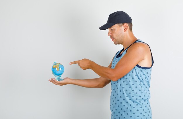 Jonge man wijzende vinger op wereldbol in blauw hemd met pet