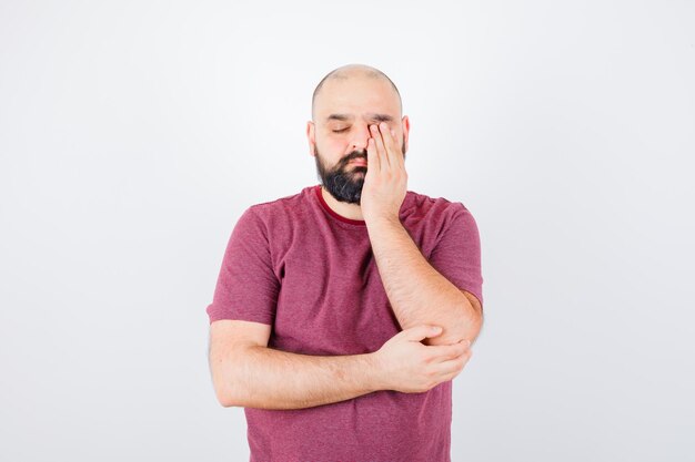 Jonge man wrijft over zijn ene oog in roze t-shirt en ziet er slaperig uit. vooraanzicht.