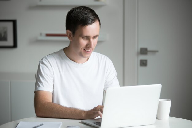Jonge man zit aan het witte bureau werken met laptop