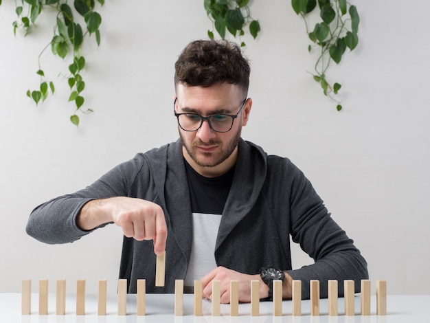 jonge man zit in bril kijkt grijze jas spelen met kleine houten figuren samen met plant op wit