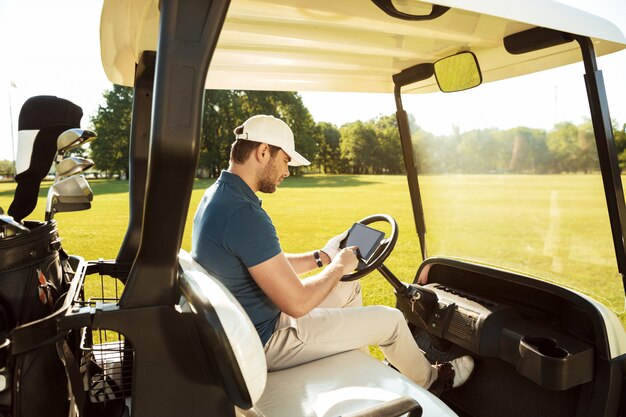 Jonge man zit in een golfkar met een tablet