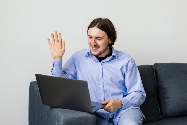 Jonge man zit op de bank en maakt videogesprek op laptop thuis