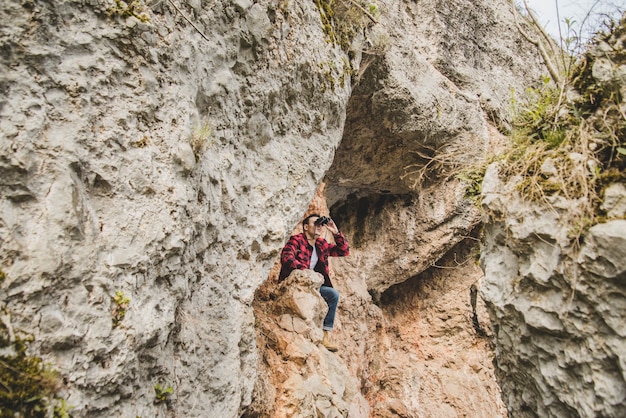 Jonge man zit op een rots en met behulp van zijn verrekijker