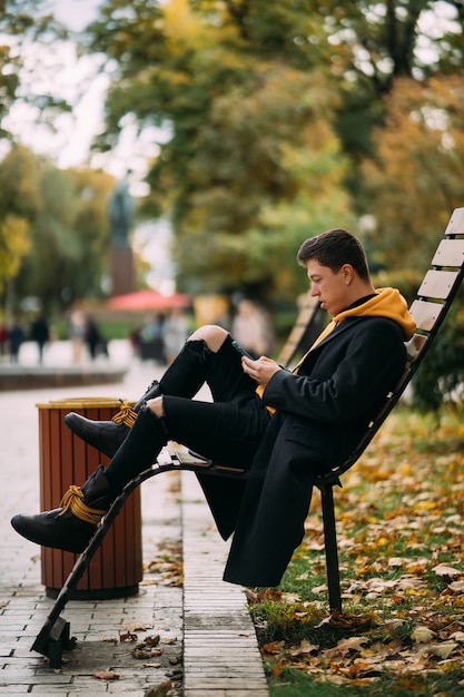 Jonge man zittend op een bankje in het park en luisteren naar muziek