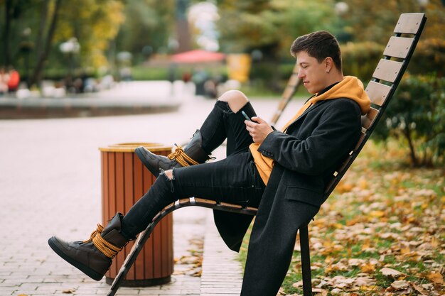 Jonge man zittend op een bankje in het park en luisteren naar muziek