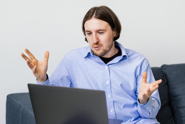 Jonge man zittend op een sofa en videogesprek voeren op laptop thuis