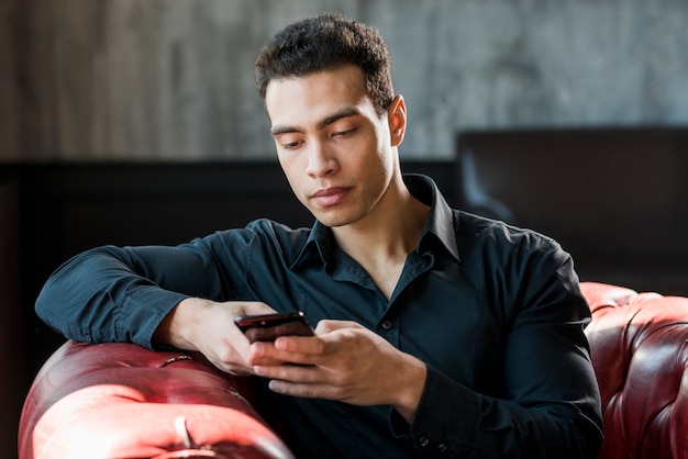 Jonge man zittend op fauteuil met behulp van de mobiele telefoon