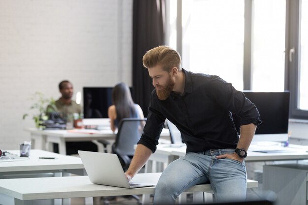 Jonge man zittend op zijn bureau en kijken naar laptop scherm