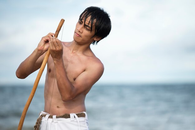 Jonge man zonder shirt op het strand met houten strik die zich voorbereidt om capoeira . te oefenen