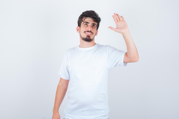 Jonge man zwaait met de hand om afscheid te nemen in t-shirt en ziet er schattig uit
