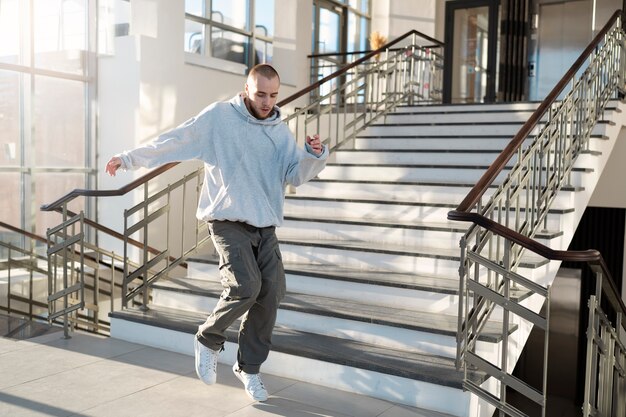 Jonge mannelijke artiest die danst in een gebouw naast trappen