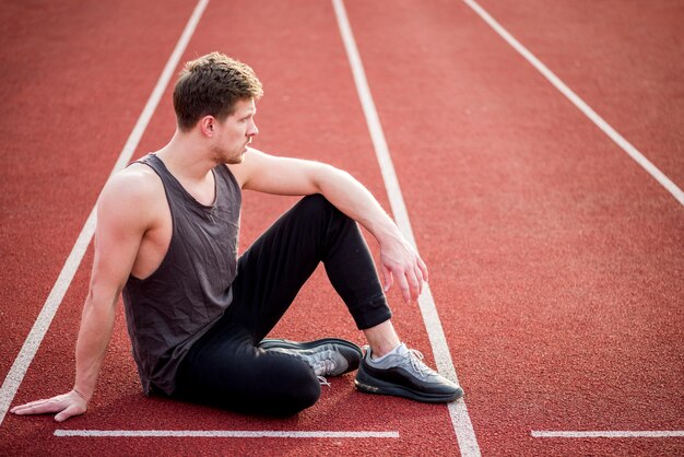 Jonge mannelijke atletenzitting op de lijn van het renbaanbegin