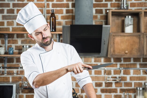 Jonge mannelijke chef-kok die scherp mes bekijkt