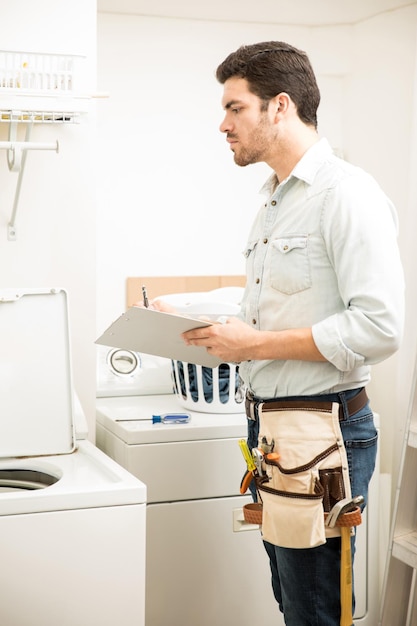 Jonge mannelijke elektricien doet wat reparaties in een wasruimte en kijkt naar een wasmachine