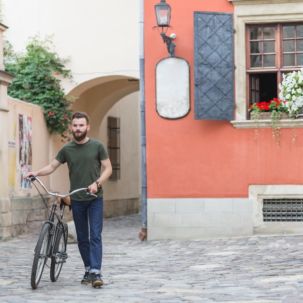 Jonge mannelijke fietser die met zijn fiets op steenbestrating loopt