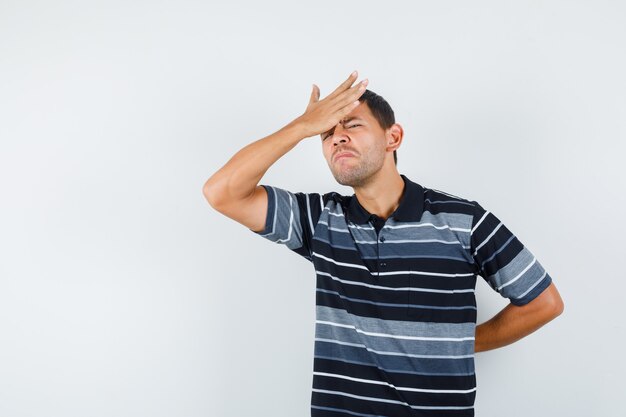 Jonge mannelijke hand op voorhoofd in t-shirt en spijtig op zoek. vooraanzicht.