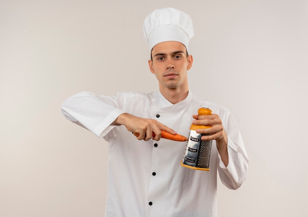 jonge mannelijke kok die chef-kok uniforme geraspte wortel op geïsoleerde witte muur draagt