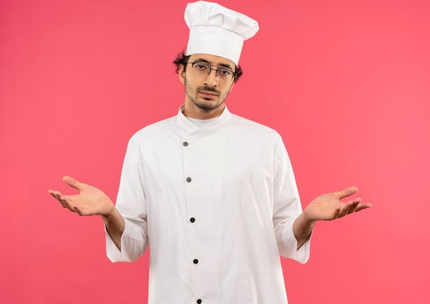jonge mannelijke kok die eenvormige chef-kok en glazen draagt die welk gebaar tonen