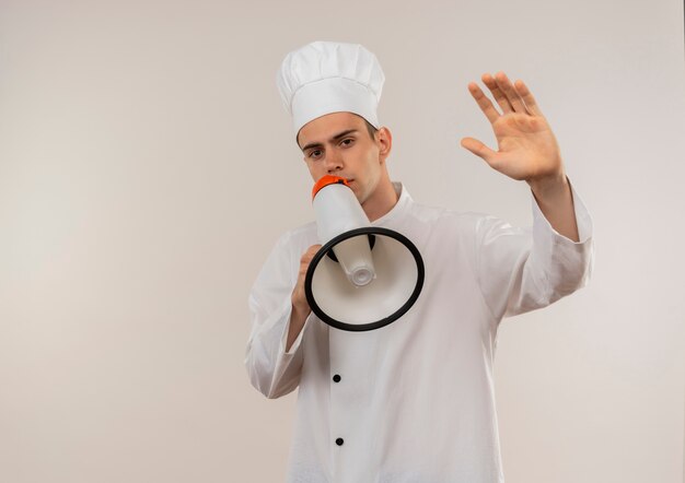 jonge mannelijke kok dragen chef-kok uniform spreekt op luidspreker stak hand op geïsoleerde witte muur met kopie ruimte