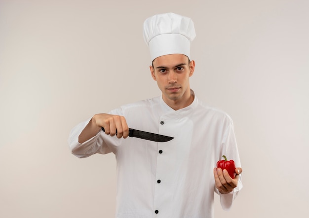 jonge mannelijke kok dragen uniforme chef-kok punten mes peper in zijn hand op geïsoleerde witte muur met kopie ruimte