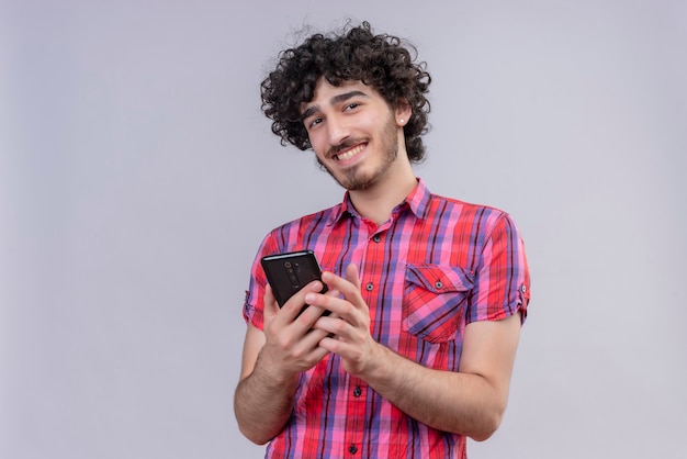 Jonge mannelijke krullend haar geïsoleerd kleurrijke shirt smartphone glimlachen