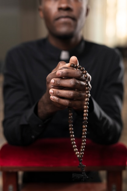 Jonge mannelijke priester bidden in de kerk met rozenkrans