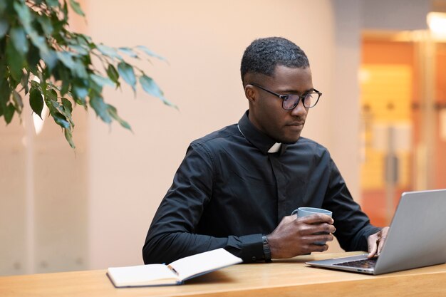Jonge mannelijke priester die laptop gebruikt in een café