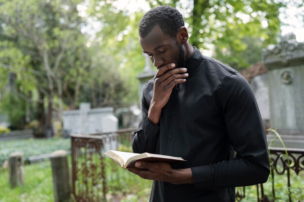 Jonge mannelijke priester met een bijbel op het kerkhof